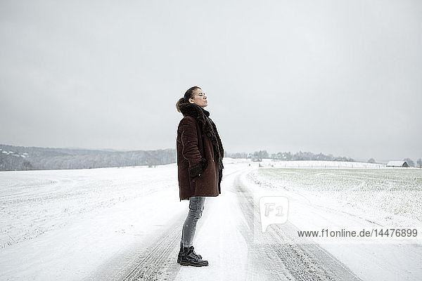 Reife Frau steht im Winter auf dem Feldweg