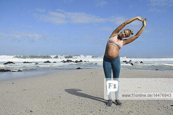 Lächelnde schwangere Frau beim Üben am Strand