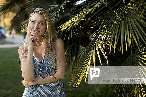Porträt einer nachdenklichen jungen Frau an einer Palme im Park
