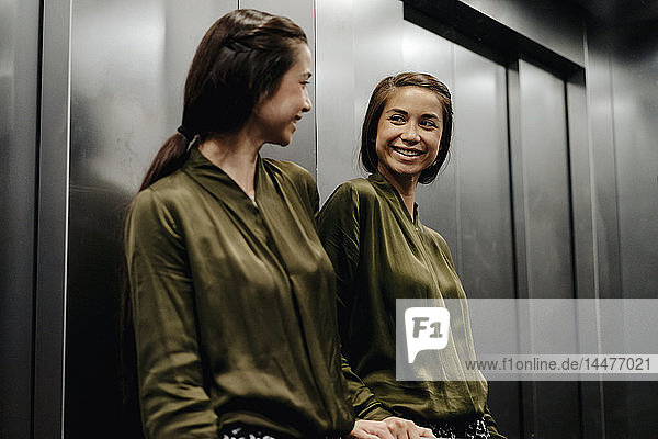 Lächelnde junge Frau schaut im Aufzug in den Spiegel
