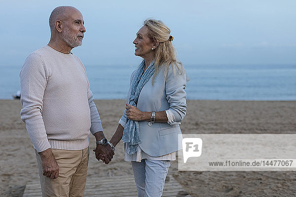 Spain  Barcelona  happy senior couple hand in hand on the beach at dusk