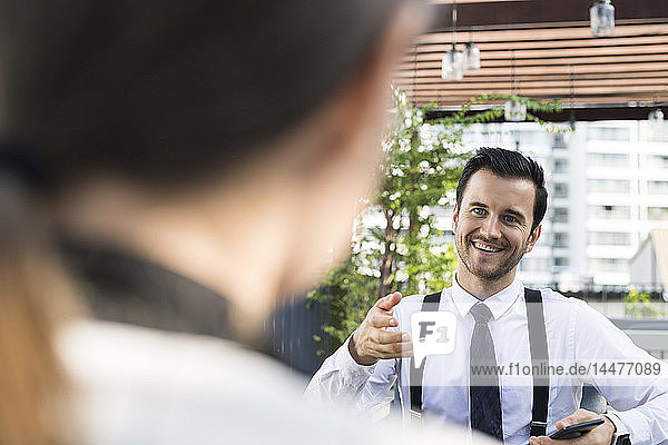 Lächelnder Geschäftsmann im Gespräch mit einem Kollegen auf der Stadtterrasse