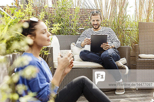 Young couple relaxing on their balcony  man sitting on couch  using laptop