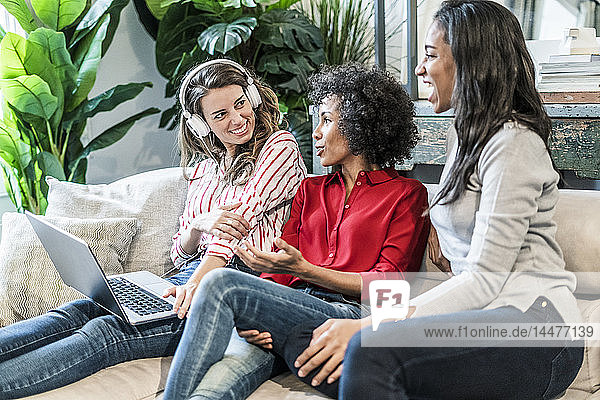 Drei glückliche Frauen mit Laptop auf der Couch sitzend