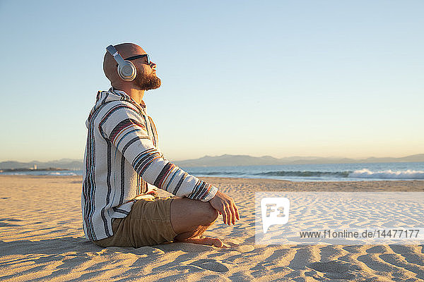 Mann mit Kopfhörern am Strand sitzend