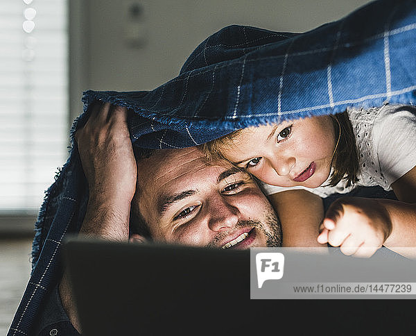 Glückliche Familie versteckt sich unter einer Decke und schaut sich einen Film auf einem Laptop an