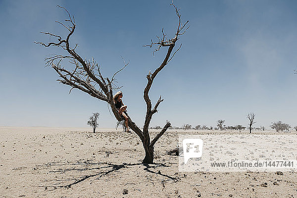 Namibia  Weg zum Sossusvlei  Frau sitzt auf einem toten Baum in der Wüste