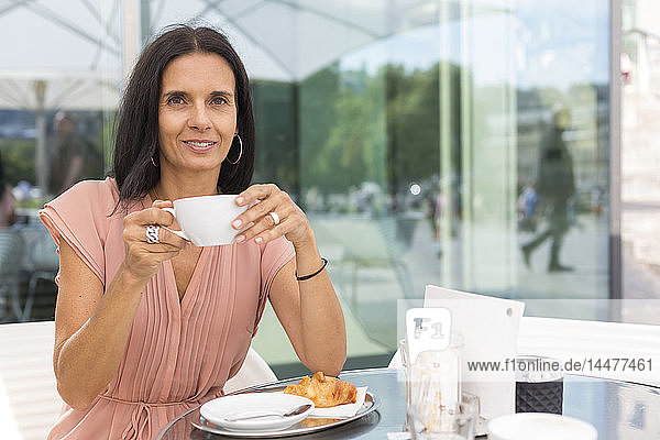 Porträt einer lächelnden reifen Frau  die im Straßencafé Kaffee trinkt