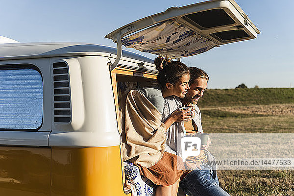 Ein glückliches Paar  das mit seinem Wohnmobil eine Reise macht  auf dem Bett sitzt und Kaffee trinkt