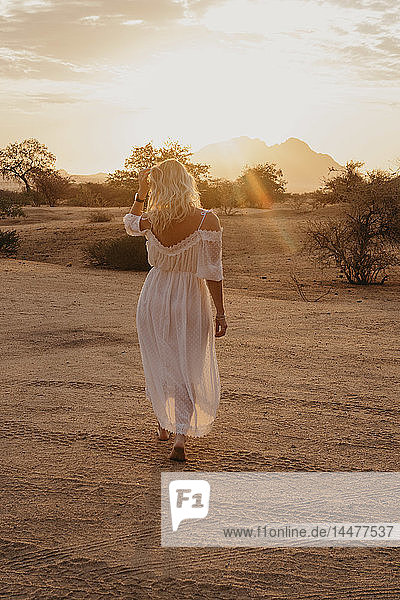 Namibia  Spitzkoppe  Rückansicht einer Frau  die bei Sonnenuntergang in einer Wüstenlandschaft spazieren geht