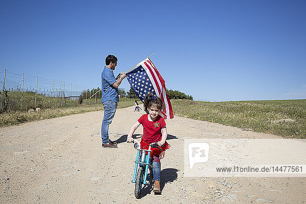 Mädchen mit Fahrrad und Mann mit amerikanischer Flagge auf Weg in entlegener Landschaft