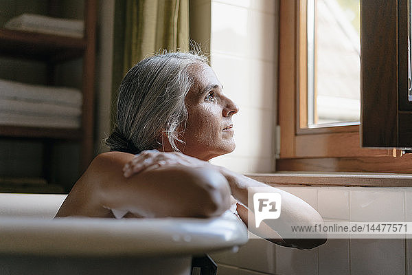 Porträt einer nachdenklichen Frau in der Badewanne  die aus dem Fenster schaut