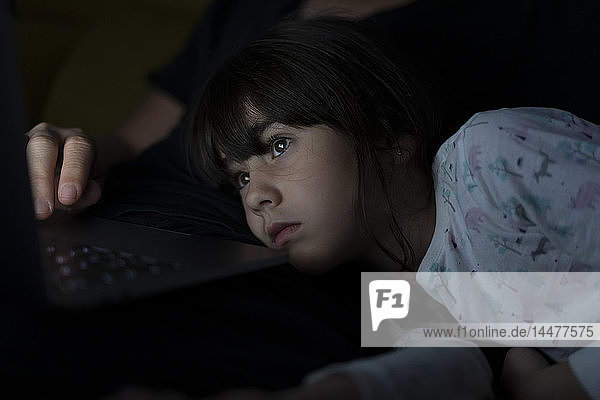 Portrait of daughter watching father using laptop on couch at night