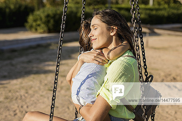 Lächelnde Mutter umarmt Tochter auf einem Spielplatz
