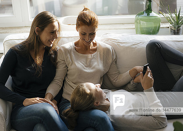 Glückliche Mutter mit zwei Teenager-Mädchen auf der Couch zu Hause mit Handy
