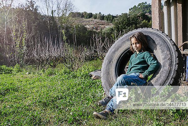 Junge sitzt in einem Autoreifen in einem Garten