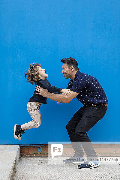 Glücklicher Vater spielt mit Sohn an blauer Wand