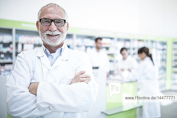 Portrait of smiling pharmacist in pharmacy with colleagues in background