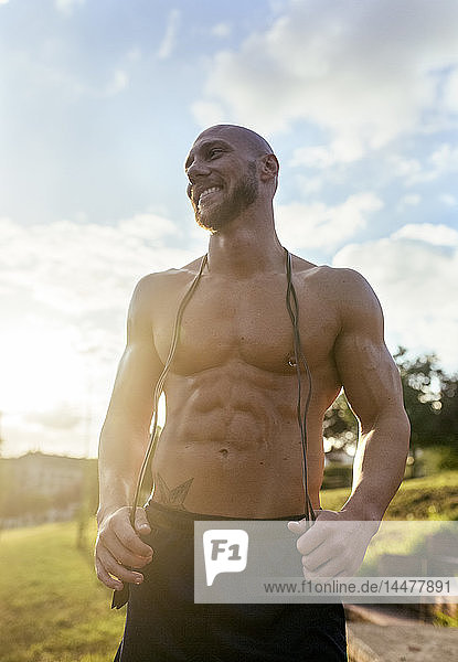 Porträt eines lächelnden  muskulösen Mannes mit freiem Oberkörper und Springseil