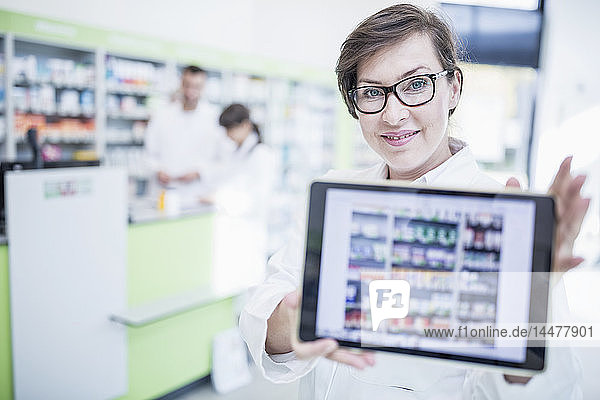 Portrait of smiling pharmacist in pharmacy showing tablet