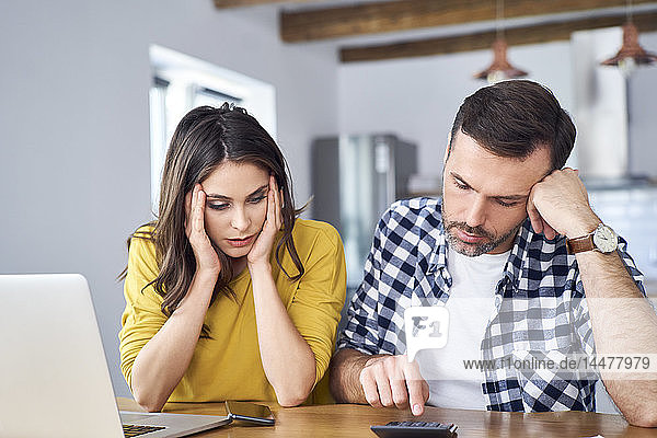 Worried couple sitting at dining table  using laptop  checking finances