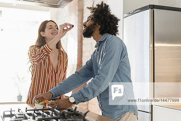 Couple standing in kitchen  preparing dinner party  woman feeding man with olive