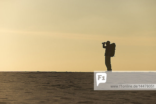 Man with backpack drinking at the beach in the evening light