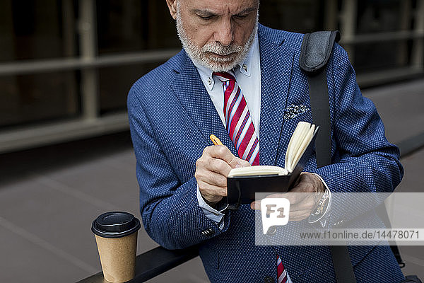 Senior businessman writing in diary outdoors