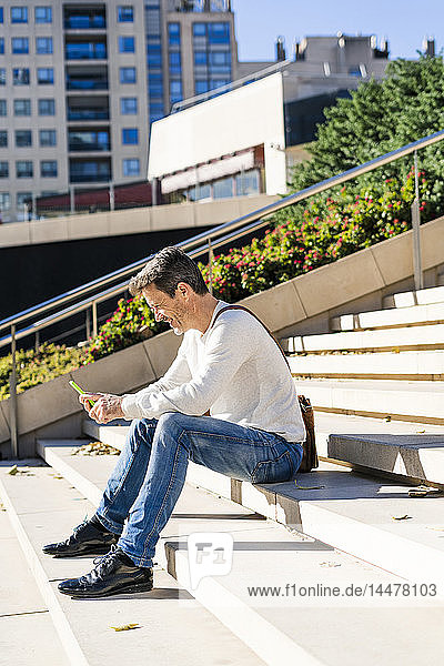 Casual businessman sitting on stairs  reading messages on his smartphone