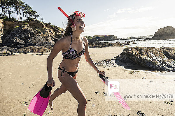 Glückliche junge Frau mit Schnorchelausrüstung  die am Strand läuft
