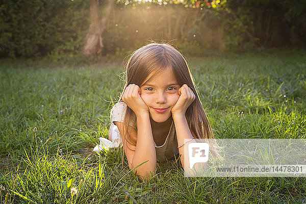 Portrait of little girl lying on a meadow at evening twilight