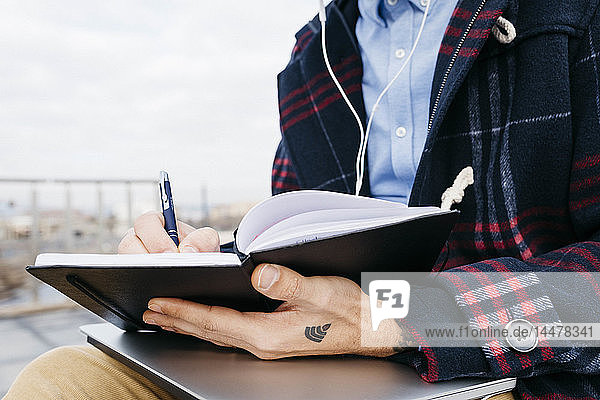 Mann mit der Tätowierung eines WiFi-Symbols auf der Hand sitzt draußen und macht Notizen