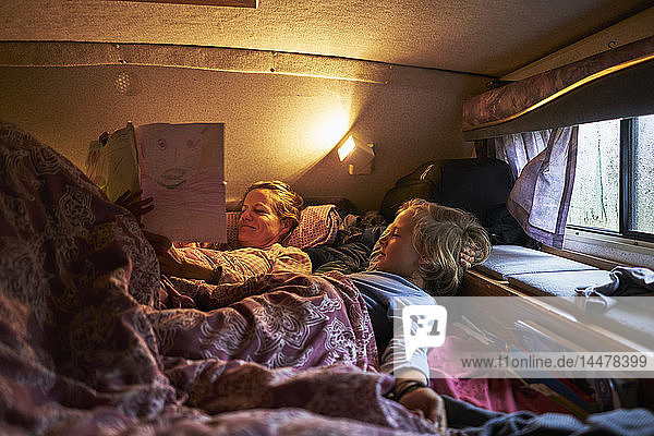 Mother looking at son's drawings lying in bed of a camper