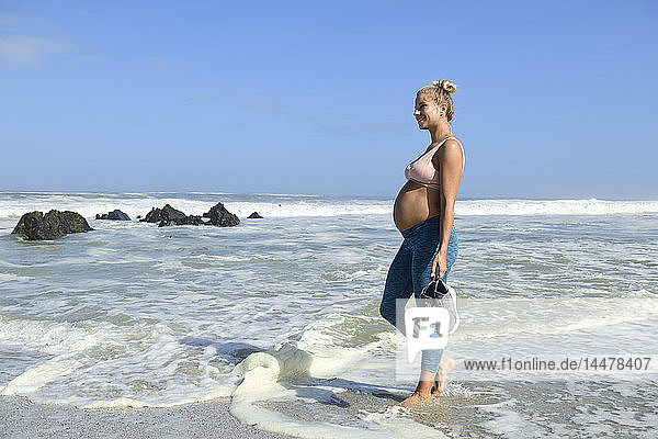 Smiling pregnant woman on the beach wading in the sea