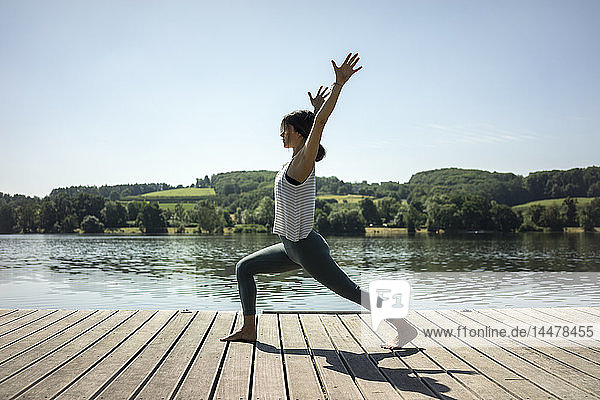 Reife Frau  die im Sommer auf einem Steg an einem See Yoga praktiziert
