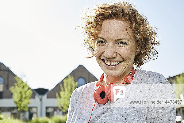 Porträt einer glücklichen jungen Frau mit Kopfhörern in städtischer Umgebung