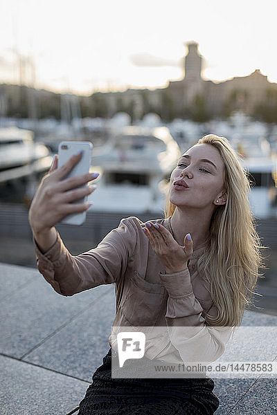 Young woman taking a selfie and blowing a kiss at the waterfront