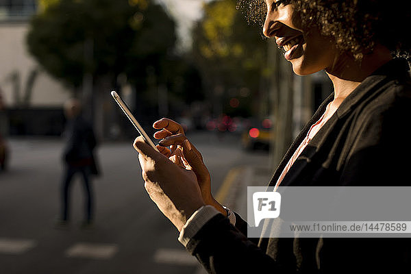Lächelnde Geschäftsfrau mit Handy auf der Straße in der Abenddämmerung  Teilansicht