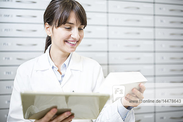 Smiling pharmacist with tablet and tablet package in pharmacy