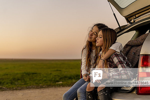 Zwei glückliche Schwestern sitzen am geöffneten Schwanz und beobachten gemeinsam den Sonnenuntergang