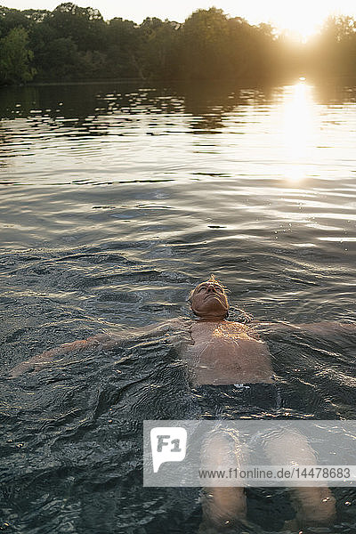 Älterer Mann schwimmt bei Sonnenuntergang in einem See