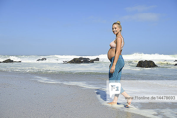 Porträt einer glücklichen schwangeren Frau am Strand  die im Meer watet