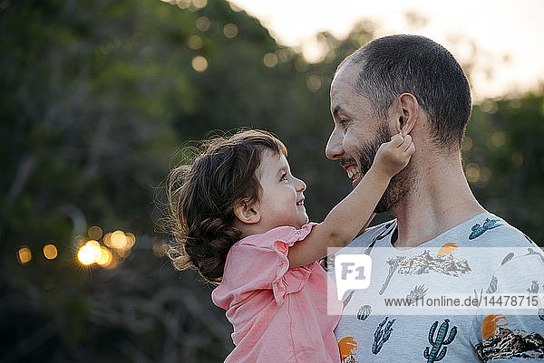 Happy father holding his daughter outdoors at sunset