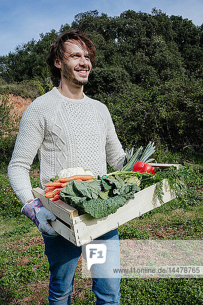 Mann trägt Kiste mit frisch geerntetem Gemüse aus seinem Gemüsegarten