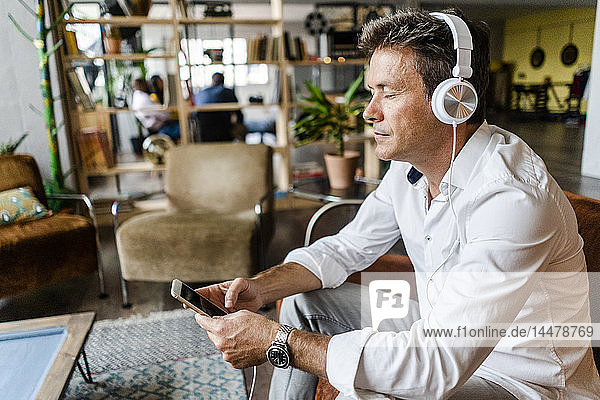 Erwachsener Mann mit geschlossenen Augen  der auf einer Couch in einem Loft Musik hört