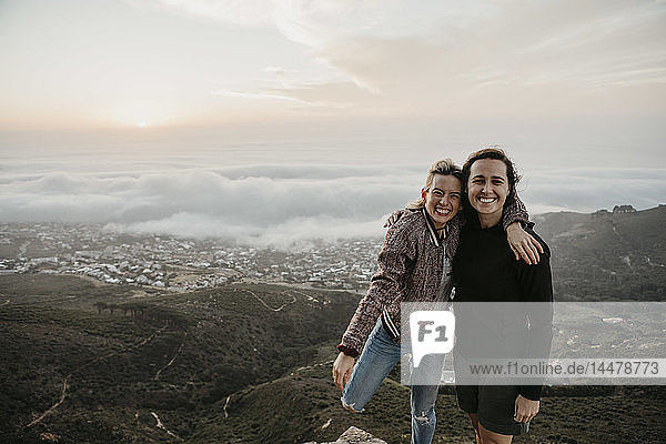 Südafrika  Kapstadt  Kloof Nek  Porträt von zwei glücklichen Frauen  die sich bei Sonnenuntergang umarmen
