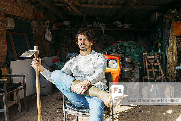 Mann mit Hacke  der mit einem Traktor in einem Schuppen sitzt