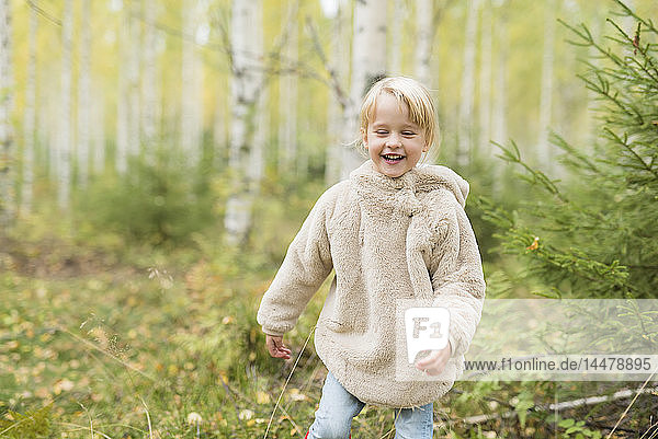 Porträt eines lachenden blonden Mädchens beim Spielen im herbstlichen Wald
