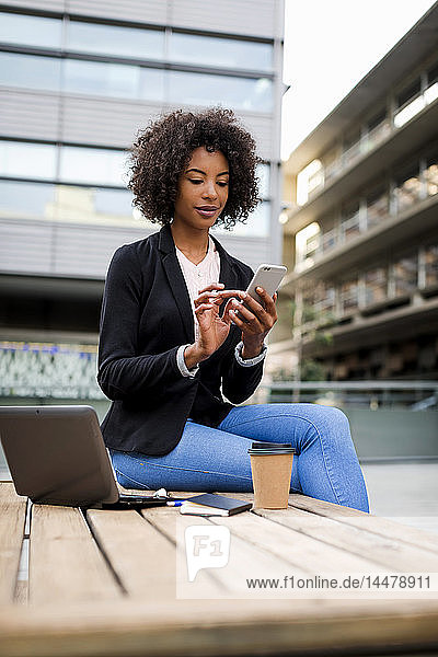 Porträt einer Geschäftsfrau  die im Freien mit einem Smartphone auf einem Tisch sitzt