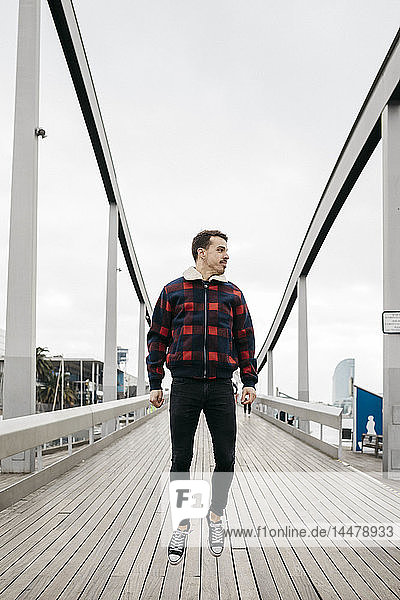 Junger Mann in legerer Kleidung springt auf eine Hafenbrücke